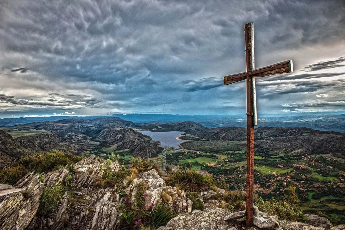 Cruzeiro no cume do Pico da Lapinha, com vista sobre a represa e o vilarejo de Lapinha da Serra sob céu nublado