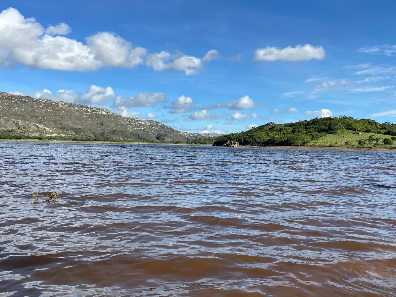 Represa cheia e com água barrenta na estação chuvosa de Lapinha da Serra, sob céu com nuvens